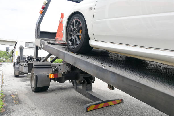 Broken down auto vehicle car towed onto flatbed tow truck with hook and chain